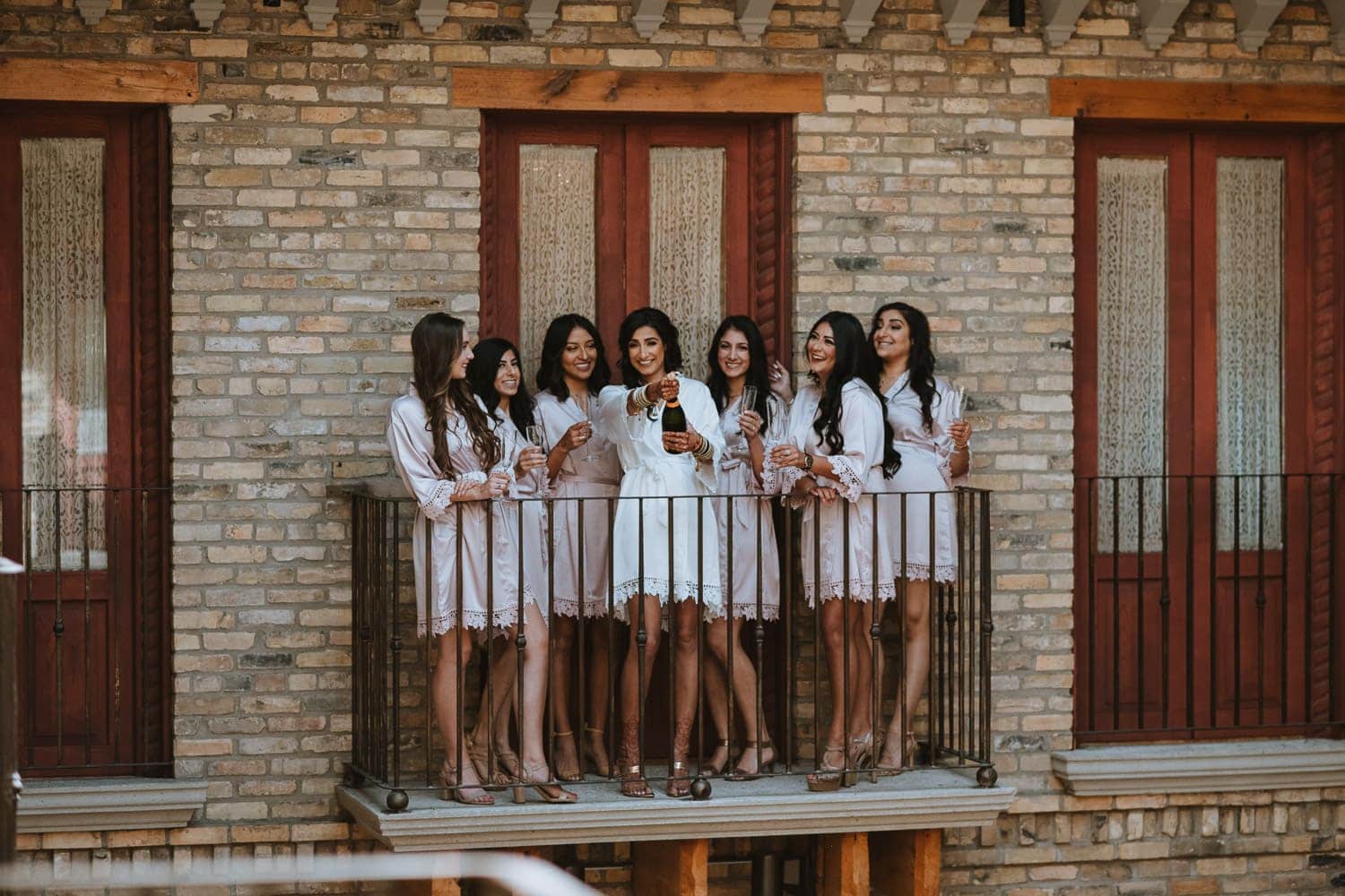 Bride and bridesmaid in night gown popping champagne at the courtyard balcony in Hacienda Sarria