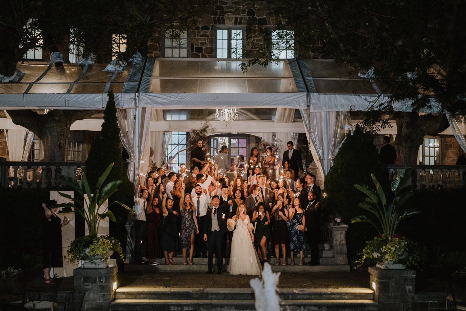 An evening photo of all wedding guests with sparklers at the fountain of Graydon Hall